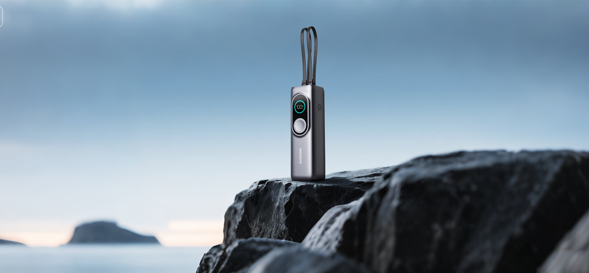 A professional product shot of the Rinecopo 170W portable power bank standing on a rugged cliffside rock overlooking the ocean. The scene highlights the durable design and integrated braided cables, making it the perfect high-capacity charging solution for travel and outdoor exploration.