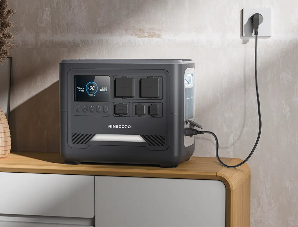 A front-side view of the Rinecopo G20 portable power station being charged via a wall outlet. Featuring a clear LCD smart display and multiple AC/DC output ports, this unit provides a seamless home emergency backup and clean energy storage solution
