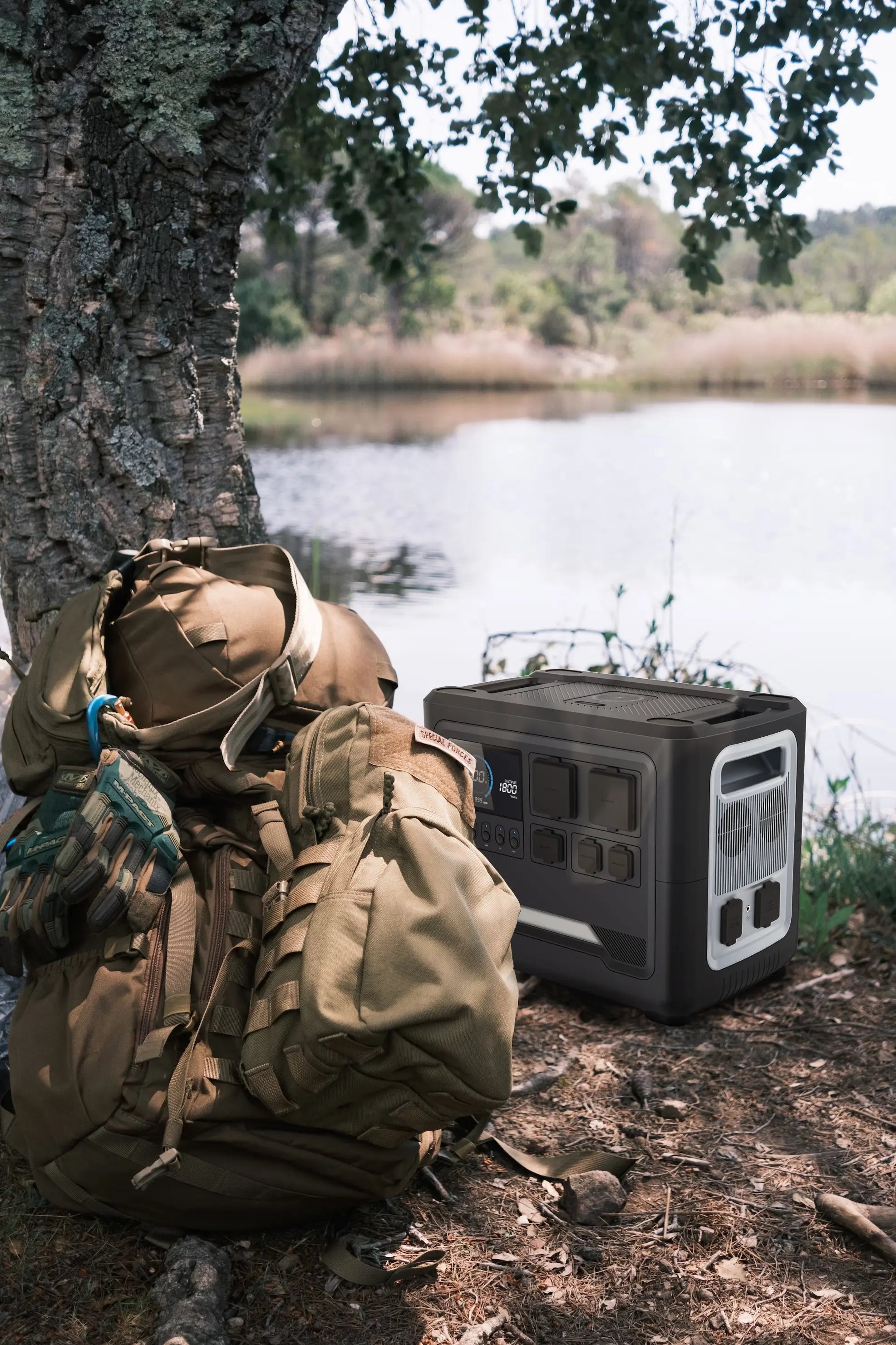 A Rinecopo portable power station paired with tactical outdoor gear and a heavy-duty backpack in a forest by a lake. This rugged solar generator is designed for wilderness survival, bushcraft adventures, and emergency preparedness in remote environments