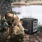 RINECOPO portable power station sitting next to a tactical backpack by a lake, providing reliable off-grid power for outdoor fishing and camping trips