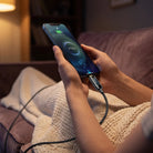 A person comfortably using their smartphone on a couch while charging with the RINECOPO smooth texture, pocket-ready USB-C cable.