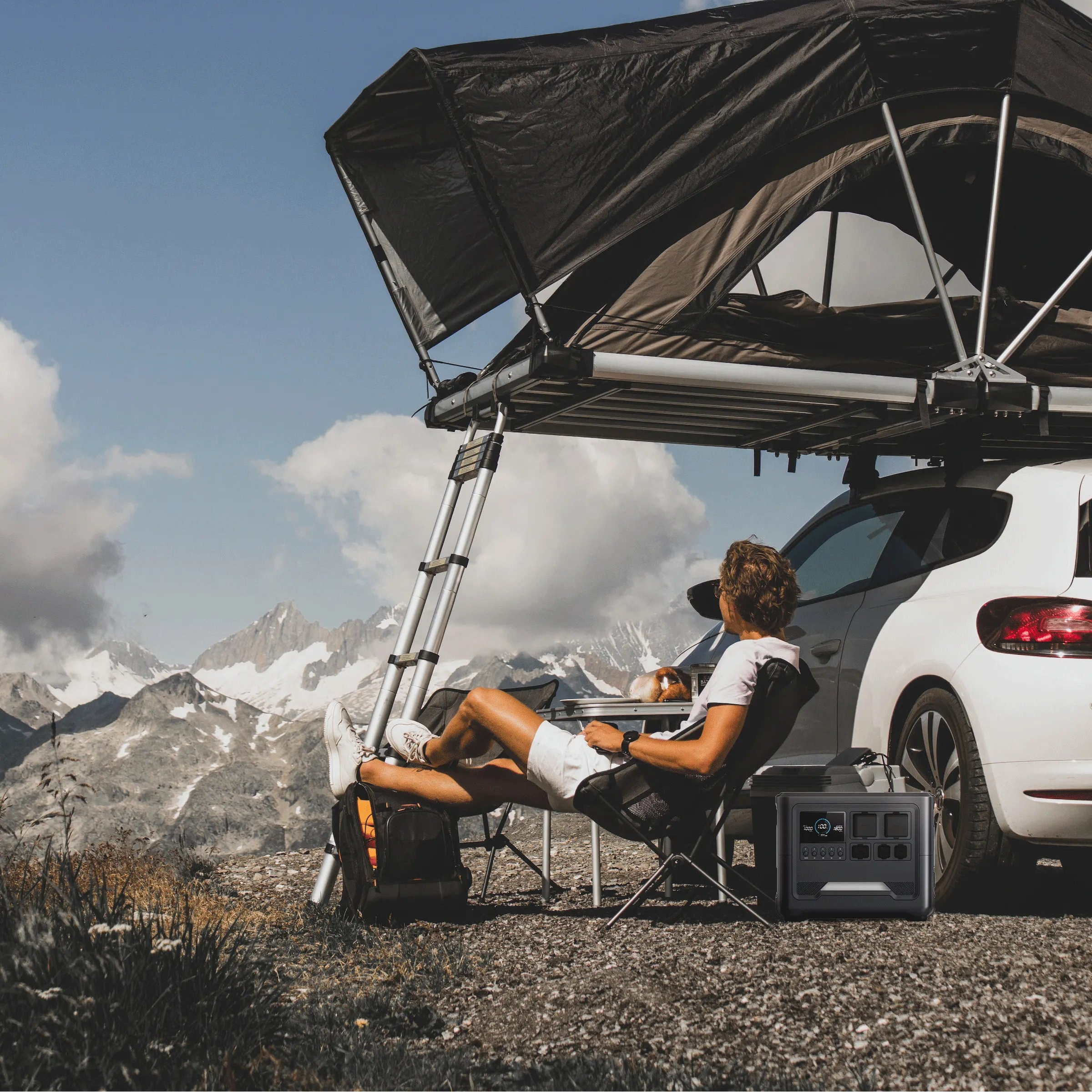 A person relaxing by their car with a roof tent in a mountainous area, powered by the rugged RINECOPO 1800W portable solar generator